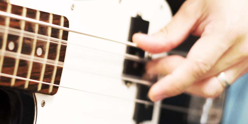 Left handed bass guitar being played, closeup of frets and pickups