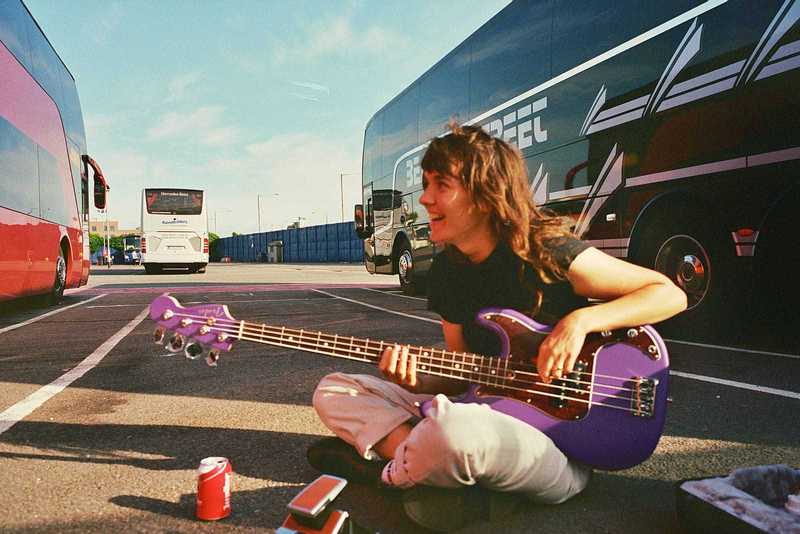 Courtney Barnett playing an upside-down right handed purple Fender Precision bass guitar.