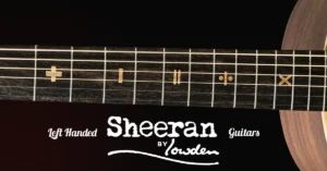 Left Handed Sheeran Guitars - The image shows a close-up of the fingerboard of a left-handed Tour Edition Sheeran Guitar, featuring unique fret markers in the shape of mathematics symbols including an addition sign, a subtraction sign, an equals symbol, a division symbol, and a multiplication sign. The "Sheeran by Lowden" logo is prominently displayed beneath the fingerboard, with the text "Left Handed" in an elegant font to the left of it, and "Guitars" to the right. The background is dark, making the intricate fretboard inlays and logo stand out clearly. The guitar's body is partially visible at the right edge of the image.