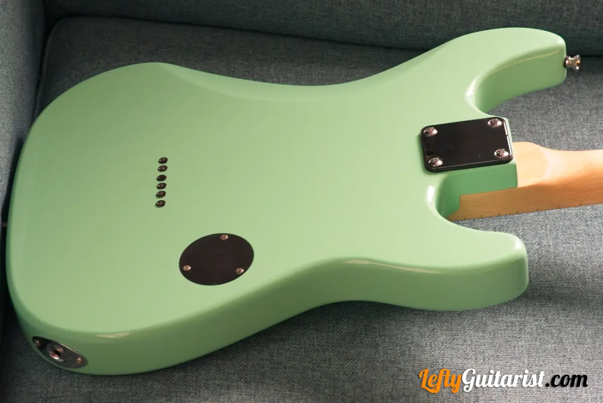 Photo of the back of a left-handed Fazley Custom Series Hot Rod V2 Electric Guitar with Fixed Bridge in a Surf Green finish. The belly cut, electronics cover, and string ferrules are visible from this angle.
