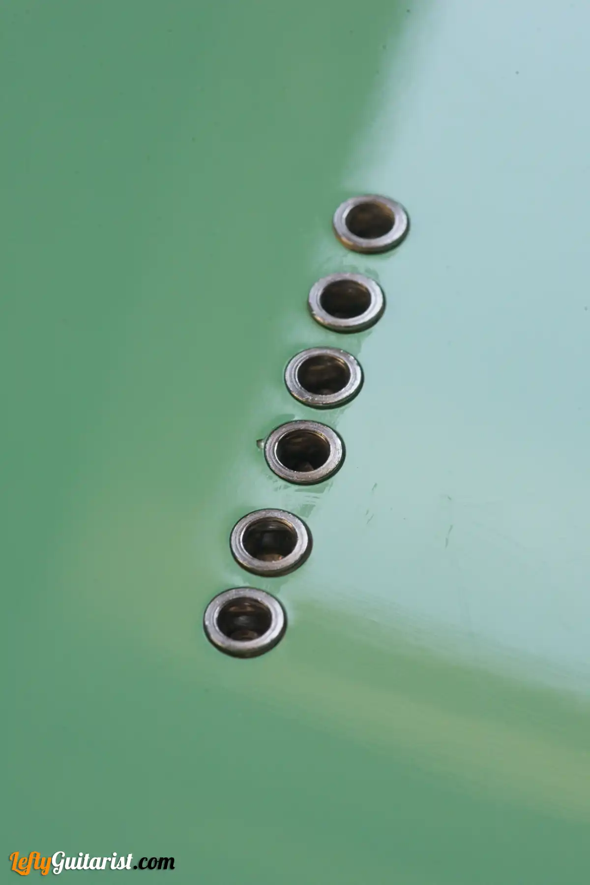 Photo of a left-handed Fazley Custom Series Hot Rod V2 Electric Guitar with Fixed Bridge in a Surf Green finish. Close-up of the string ferrules on the back of the guitar body.