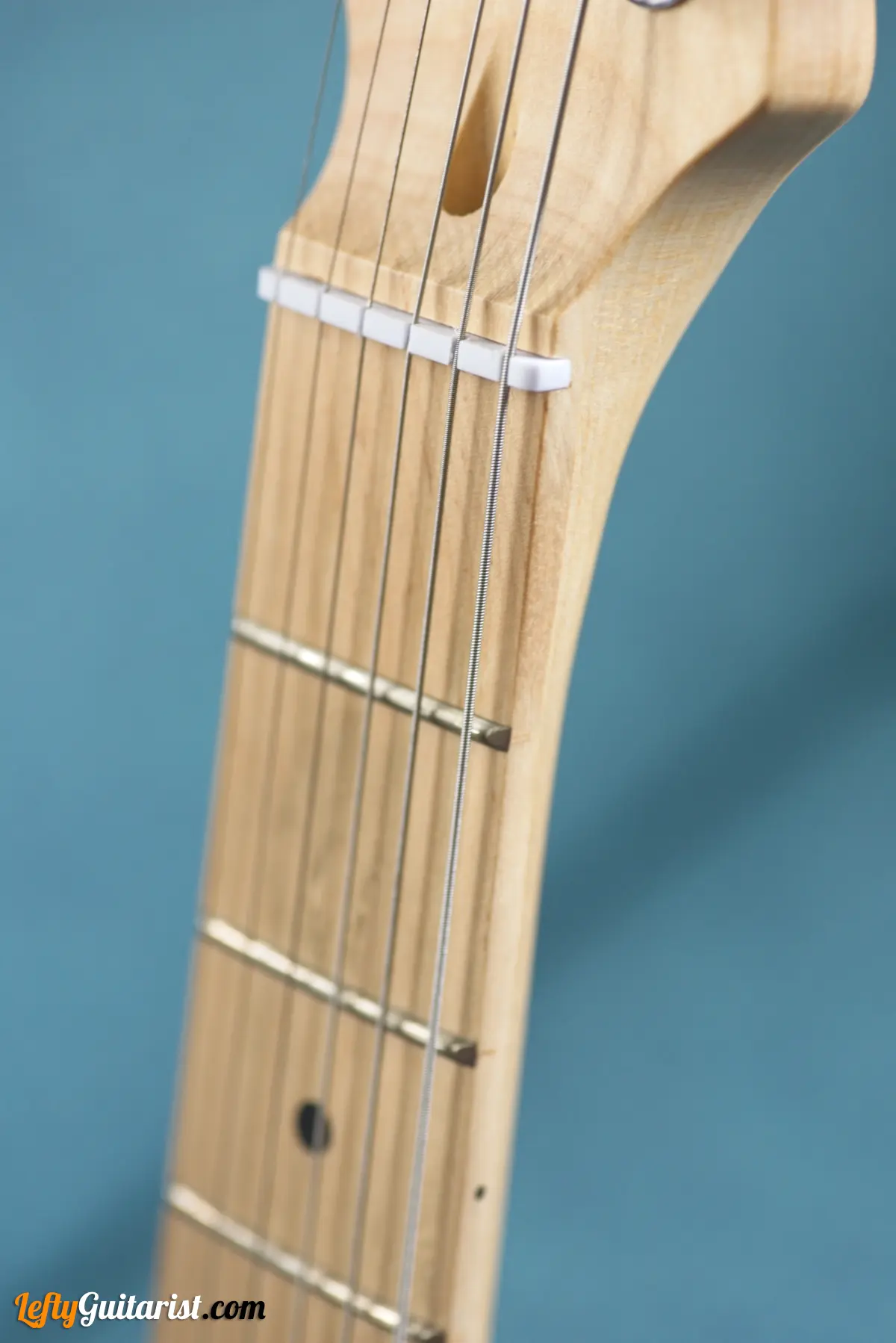 Photo of a left-handed Fazley Custom Series Hot Rod V2 Electric Guitar with Fixed Bridge in a Surf Green finish. Close-up of the nut and lower frets.